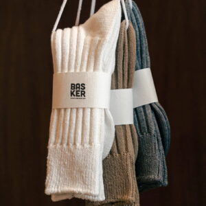 Three pairs of urban ribbed crew socks in grey, brown, and white, hanging on a line.